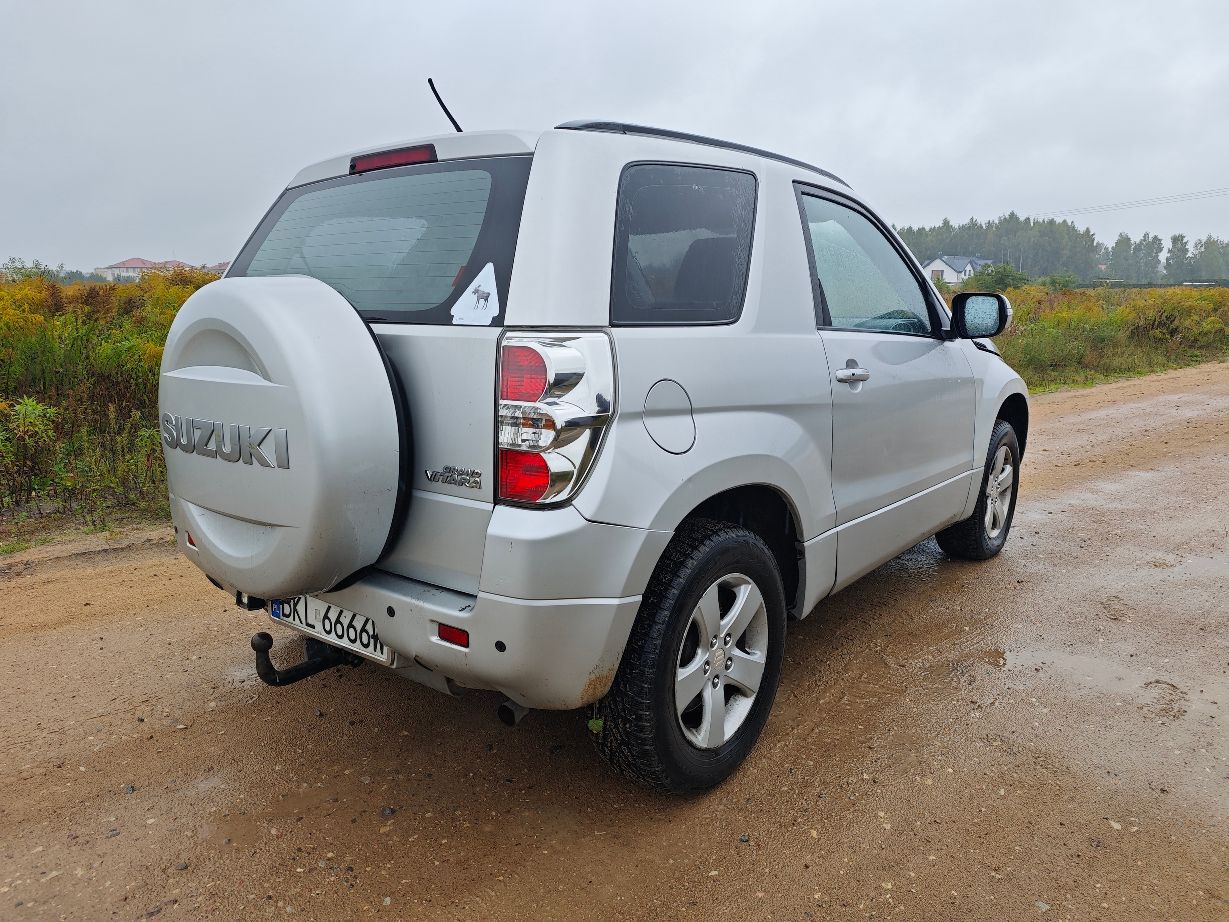 Srebrny samochód marki Suzuki Grand Vitara II w wersji trzydrzwiowej, prawy tylni bok