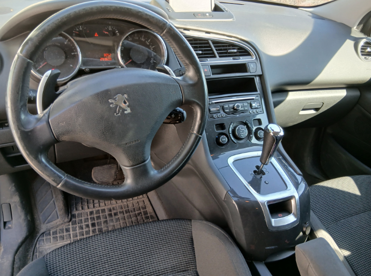 Wnętrze czarnego Peugeota 5008 z uwidocznionym brakiem radia samochodowego oraz zabrudzeniem tapicerki