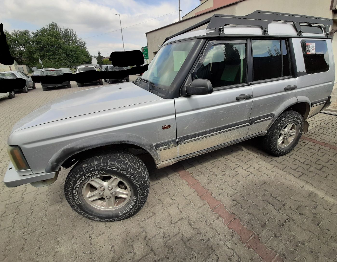 Samochód Land Rover terenowy typu SUV srebrny z czarnymi elementami nadwozia. Ma terenowe opony i aluminiowe felgi.