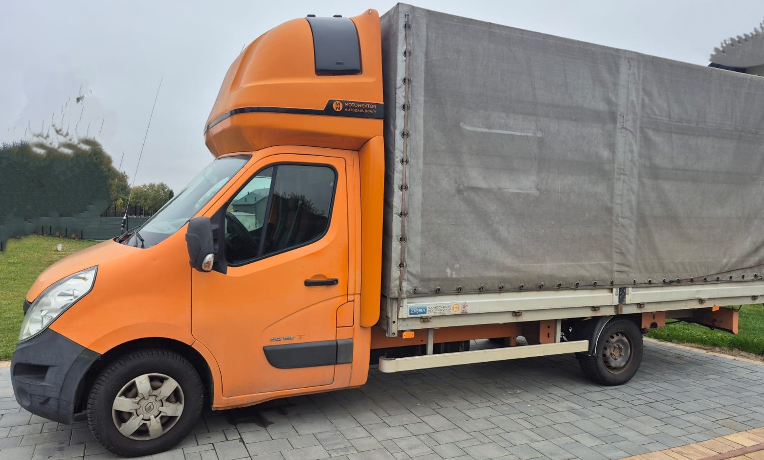 Lewa strona pojazdu Renault Master koloru pomarańczowego z szarą plandeką.