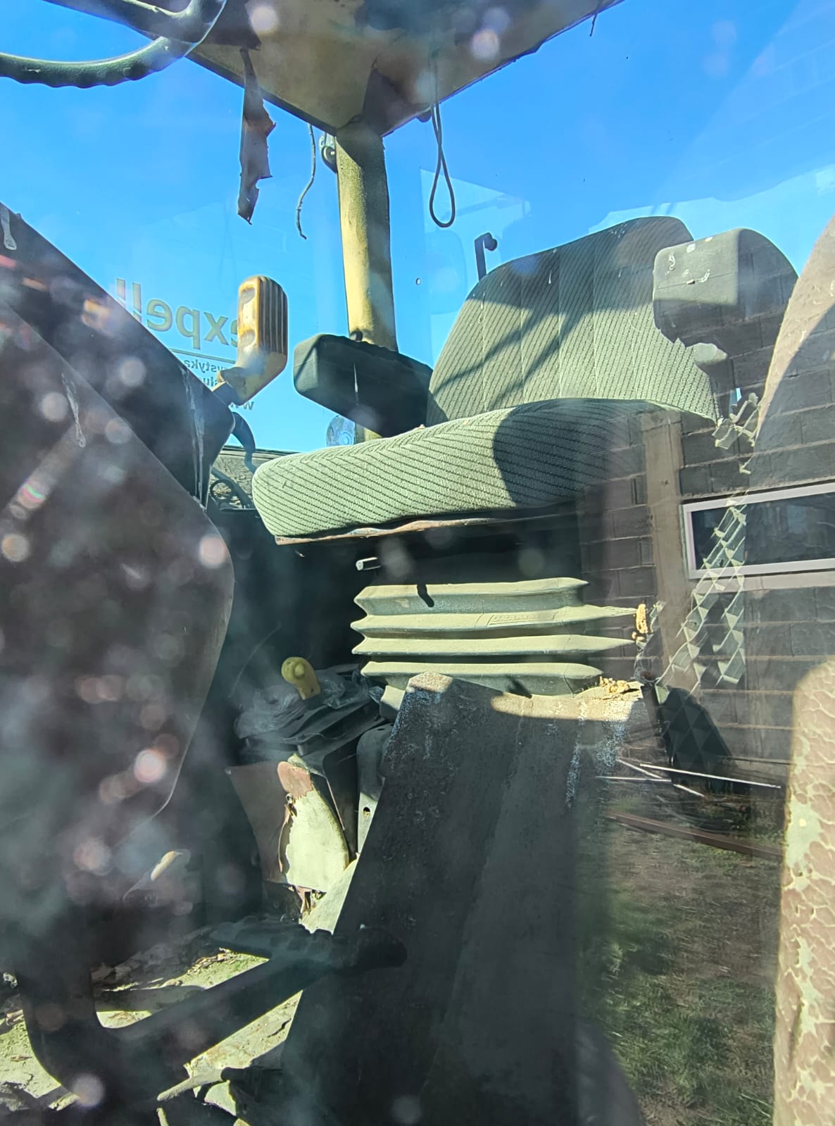 fotografia przedstawia zużyty fotel operatora z zieloną, materiałową tapicerką w paski oraz ciemnymi podłokietnikami.