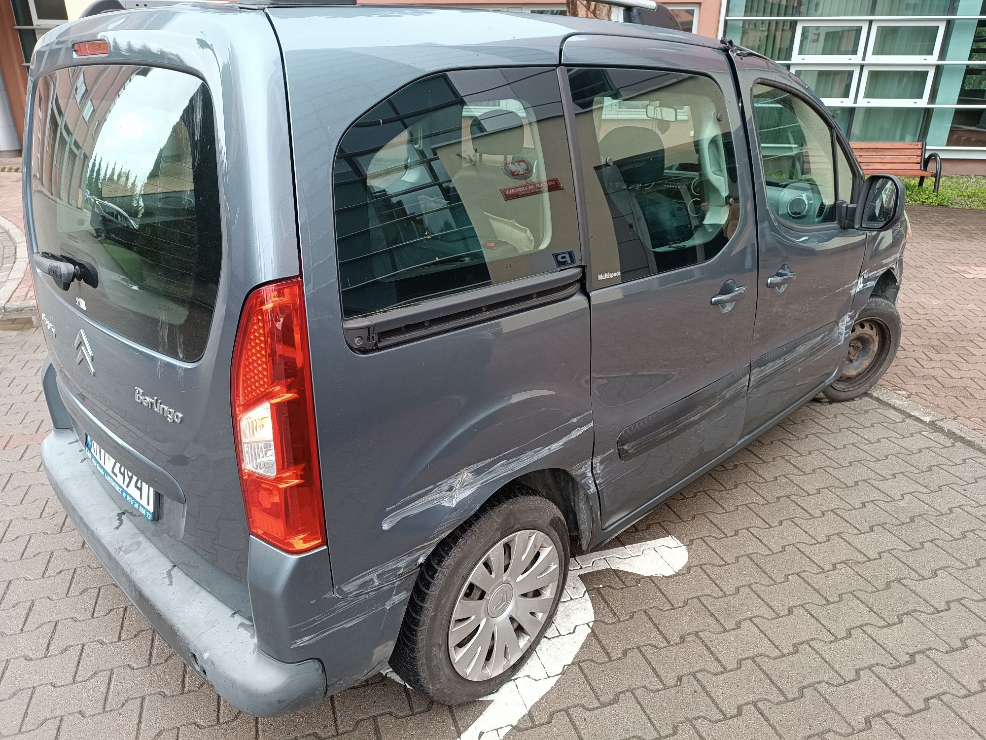Uszkodzony samochód osobowy marki Citroën Berlingo; widoczne są zarysowania i wgniecenia na tylnych drzwiach