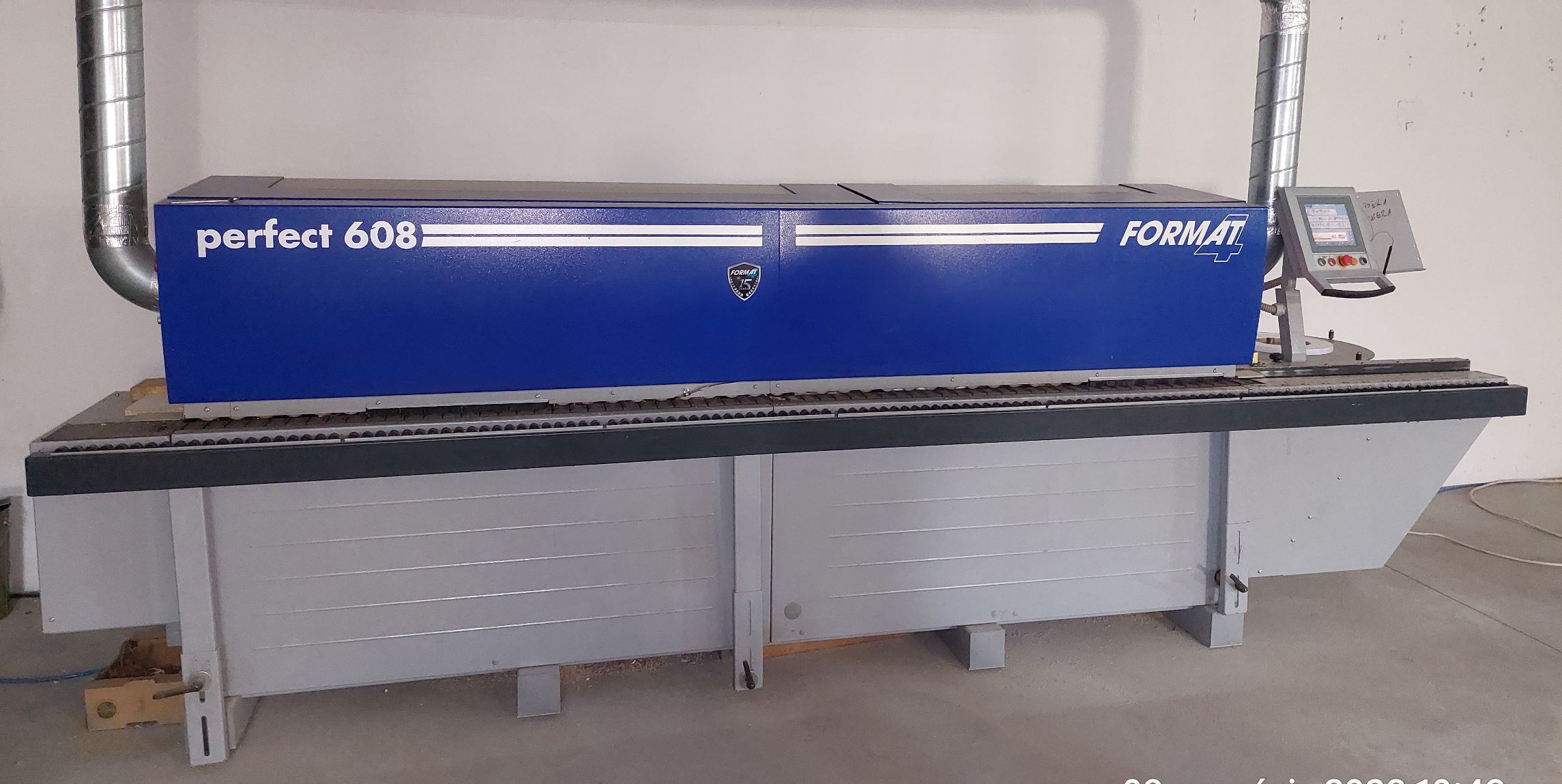 Okleiniarka koloru szaro niebieskiego. Napis perfekt 608 Format 4 w górnej części maszyny. Po prawej stronie panel do obsługi.