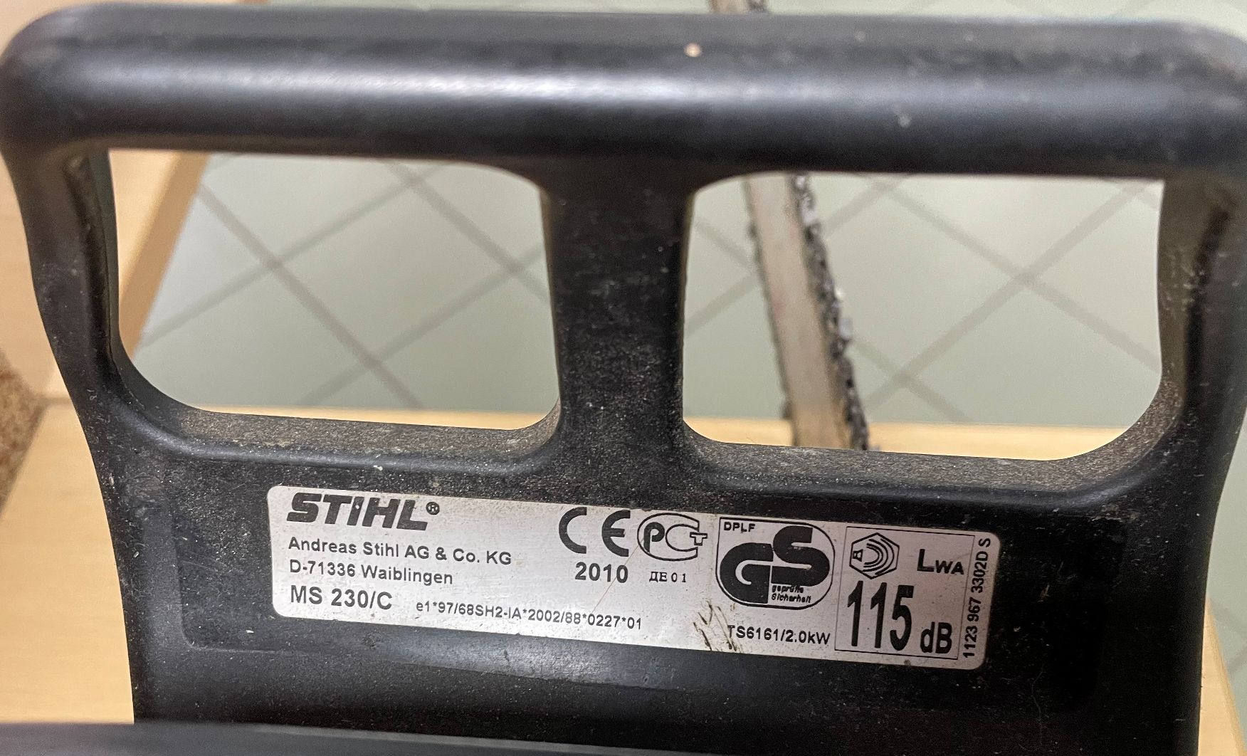 Osłona hamulca pilarki STIHL MS 230/C ze srebrną naklejką znamionową, na której widnieje rok produkcji 2010 i dane techniczne