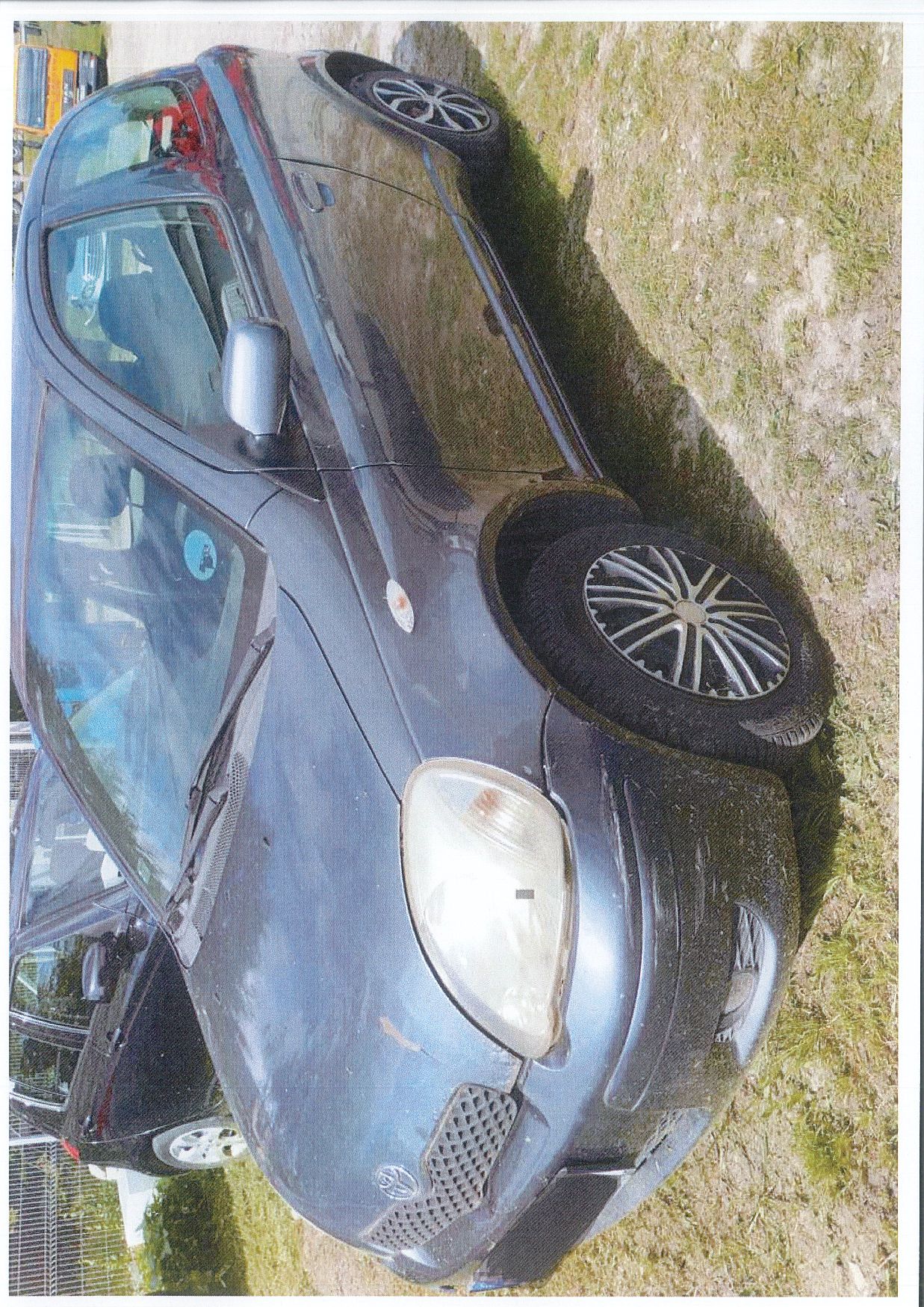 Lewa strona samochodu osobowego TOYOTA YARIS, zderzak z przodu mocno porysowany, wypięty. Lakier uszkodzony, widoczna korozja.