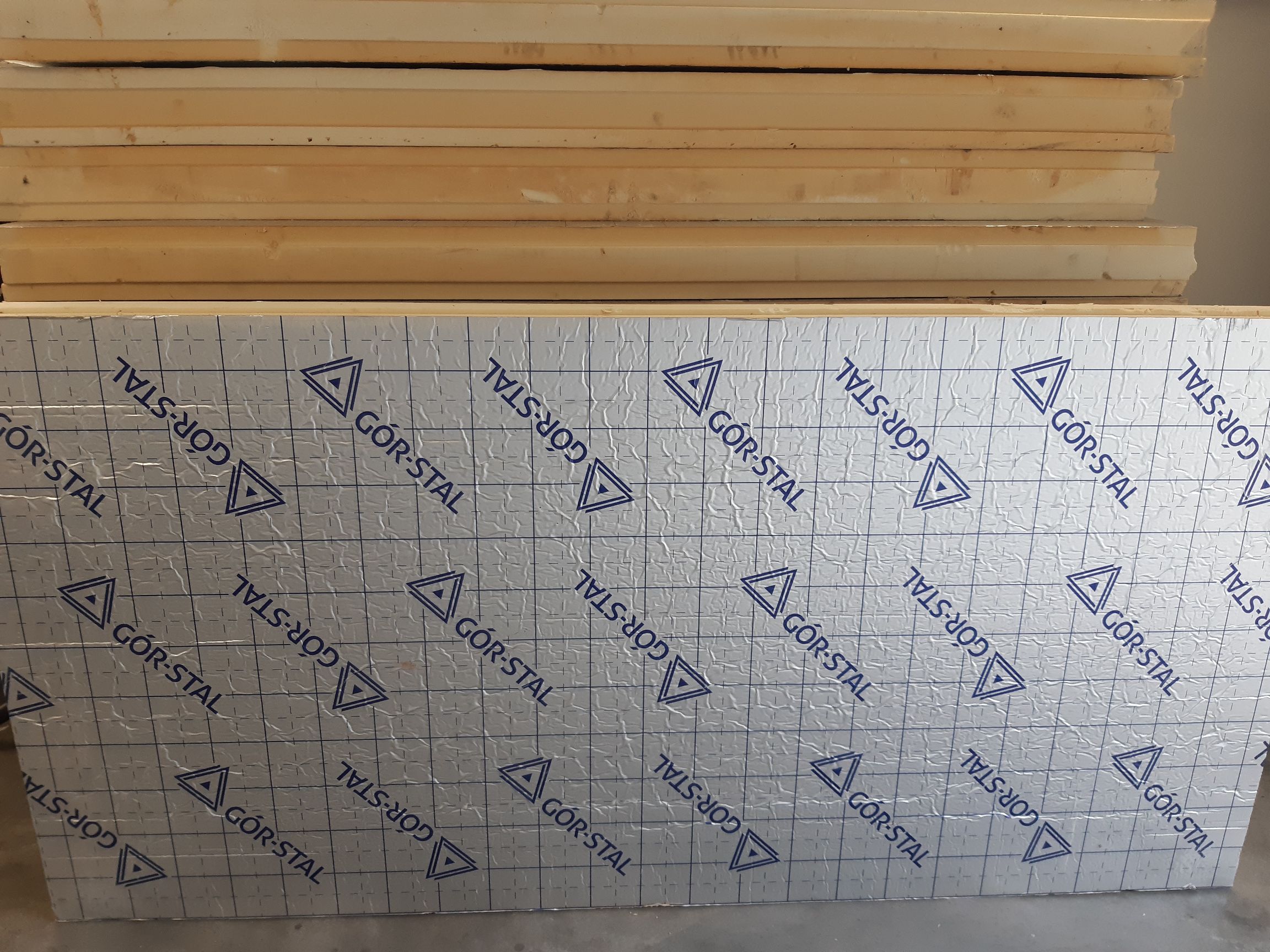 Stos białych płyt izolacyjnych. Na przedniej płycie znajduje się srebrzysta folia ochronna z nazwą producenta.