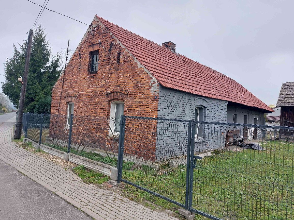 Widok frontowy wolnostojącego domu jednorodzinnego z czerwonej cegły, położonego na ogrodzonej działce
