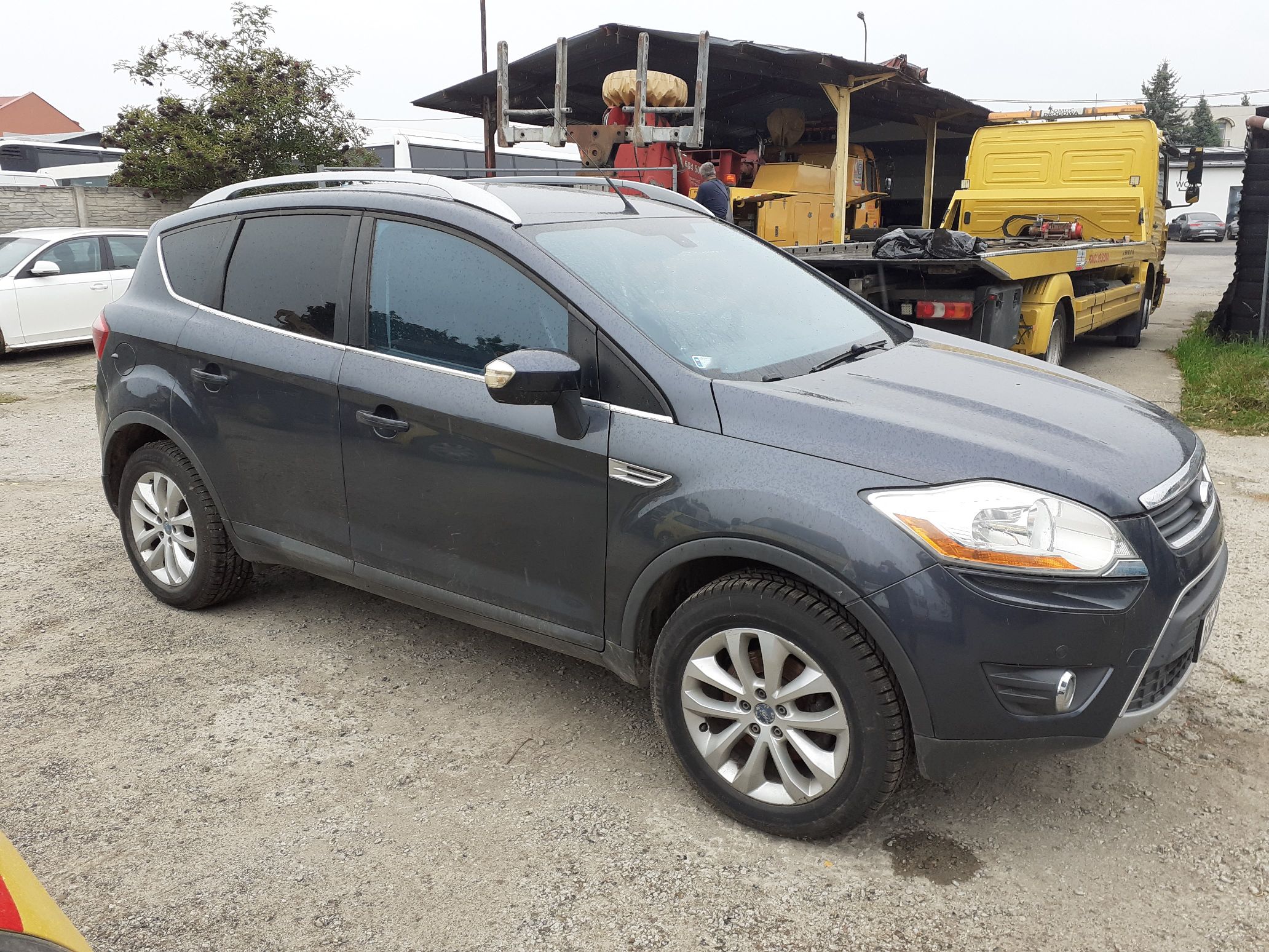 Czarny Ford Kuga widok z boku od strony pasażera. Widoczne przyciemniane tylne szyby, aluminiowe koła i srebrne relingi dachowe.