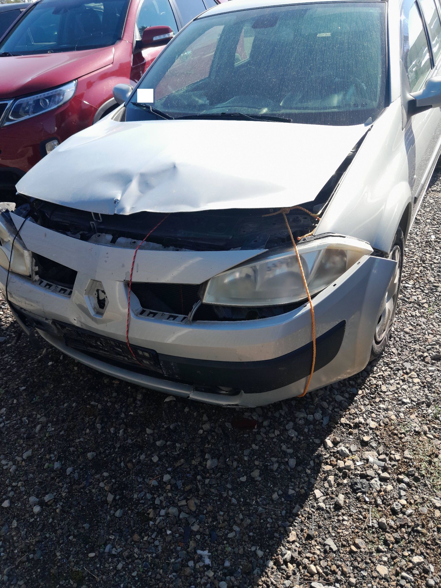 Srebrne Renault Megane z uszkodzonym przodem pojazdu po wypadku widziane z przodu.