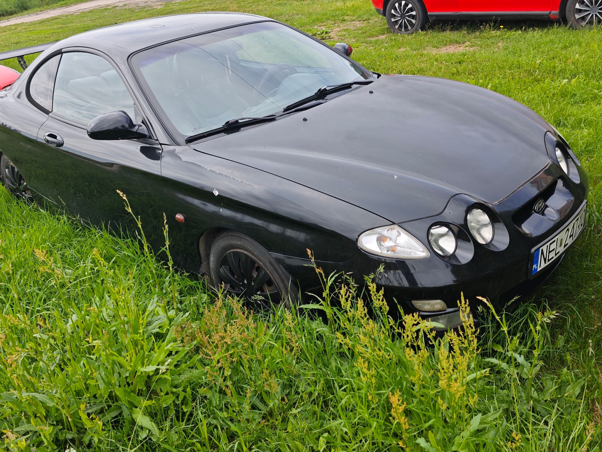 Czarny dwudrzwiowy Hyundai coupe, charakterystyczne podwójne okrągłe reflektory, czarne felgi oraz tylny spojler.