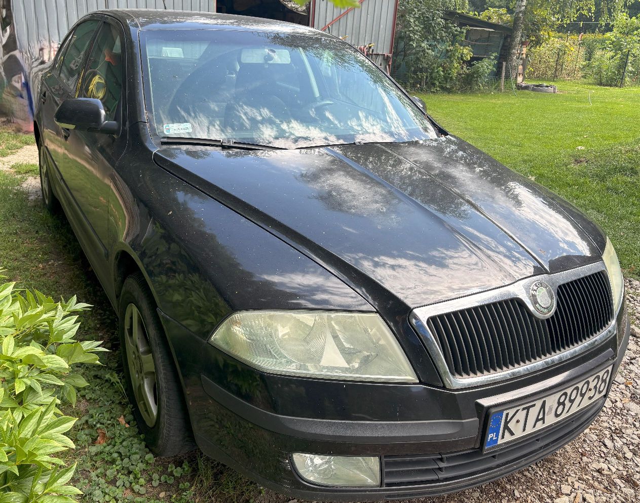 Przód czarnego samochodu osobowego marki Skoda Octavia drugiej generacji . Reflektory samochodu są lekko zmatowiałe.