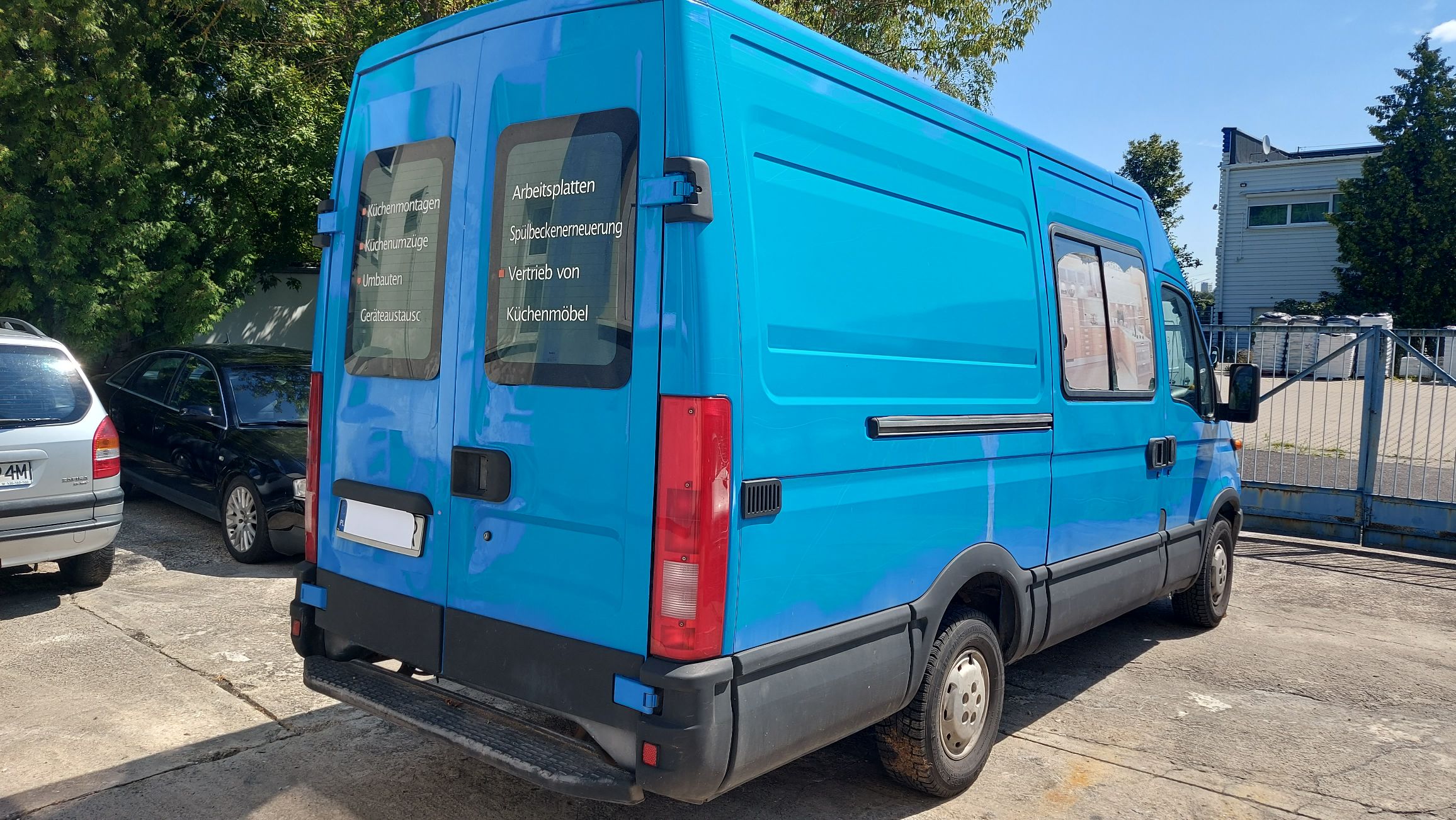 Tył i prawy bok jasnoniebieskiego Iveco Daily z napisami reklamowymi na tylnych drzwiach.