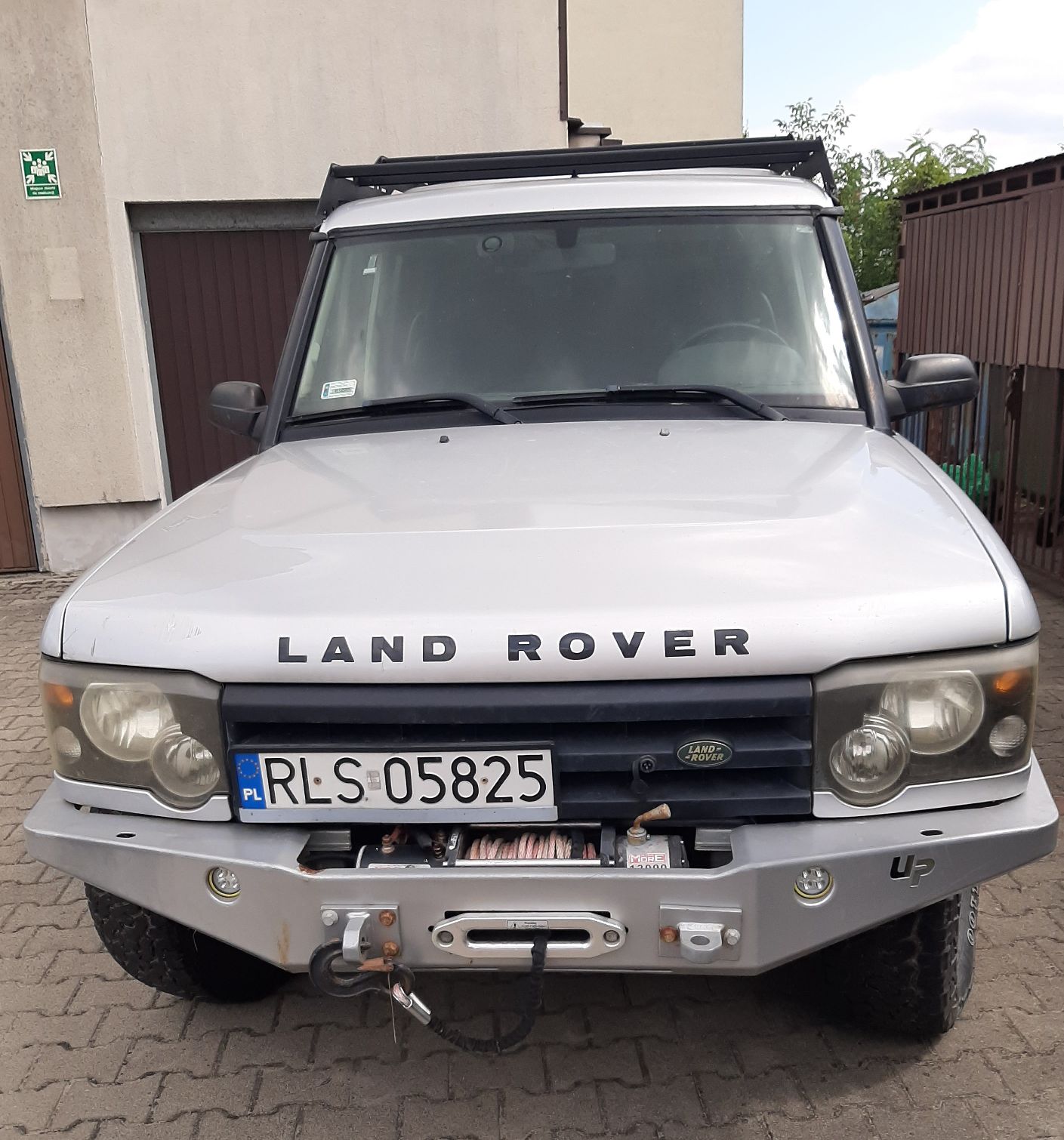 Samochód Land Rover terenowy typu SUV srebrny. Z przodu zamontowano wzmocniony metalowy zderzak z wyciągarką.