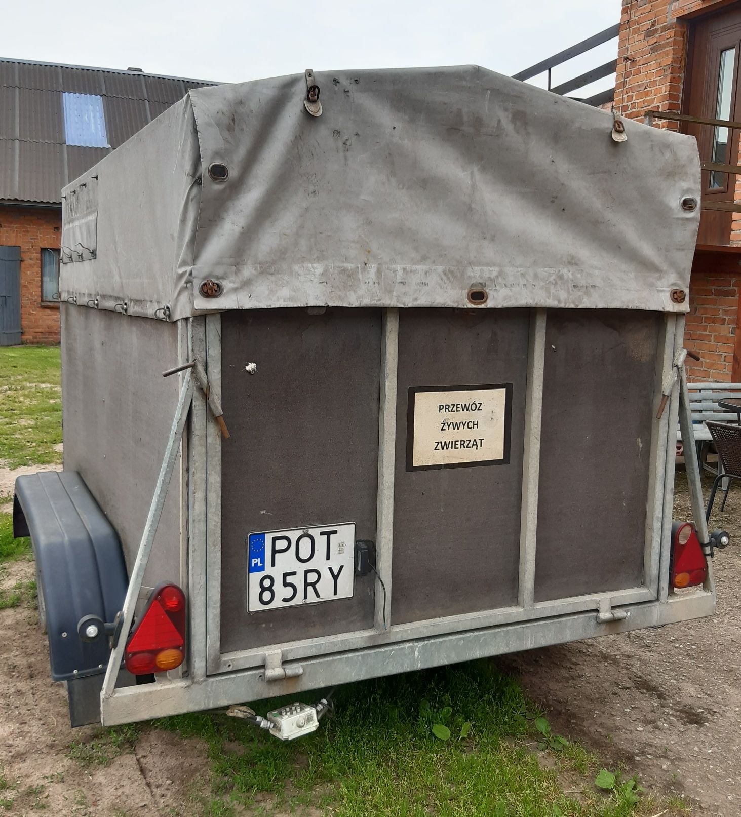 Tył szarej, zakrytej przyczepy do transportu żywych zwierząt, posiadająca metalowy stelaż.