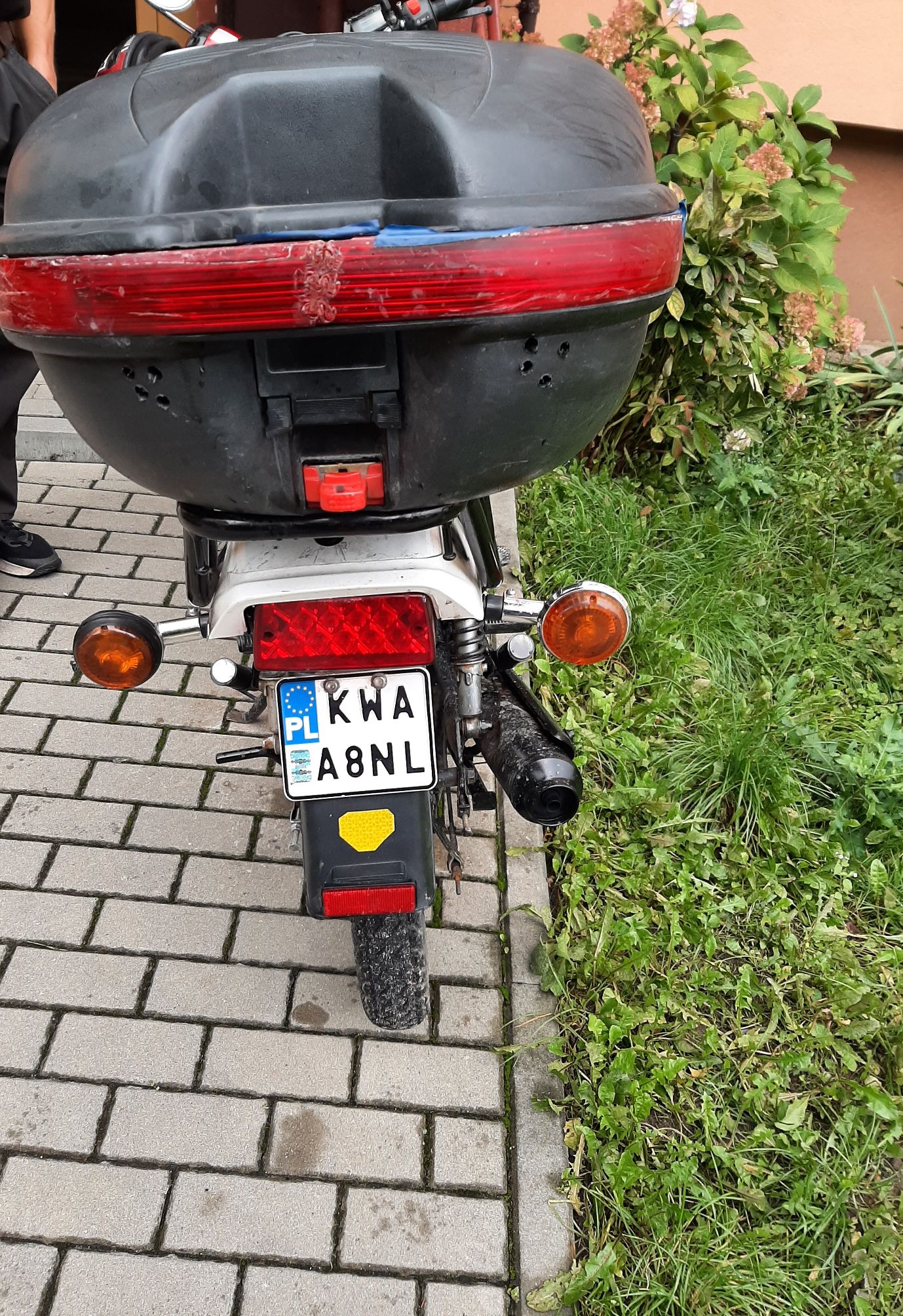 Tył motoroweru Romet Chart 50 z dużym kufrem centralnym, czerwonym światłem tylnym i pomarańczowymi kierunkowskazami.