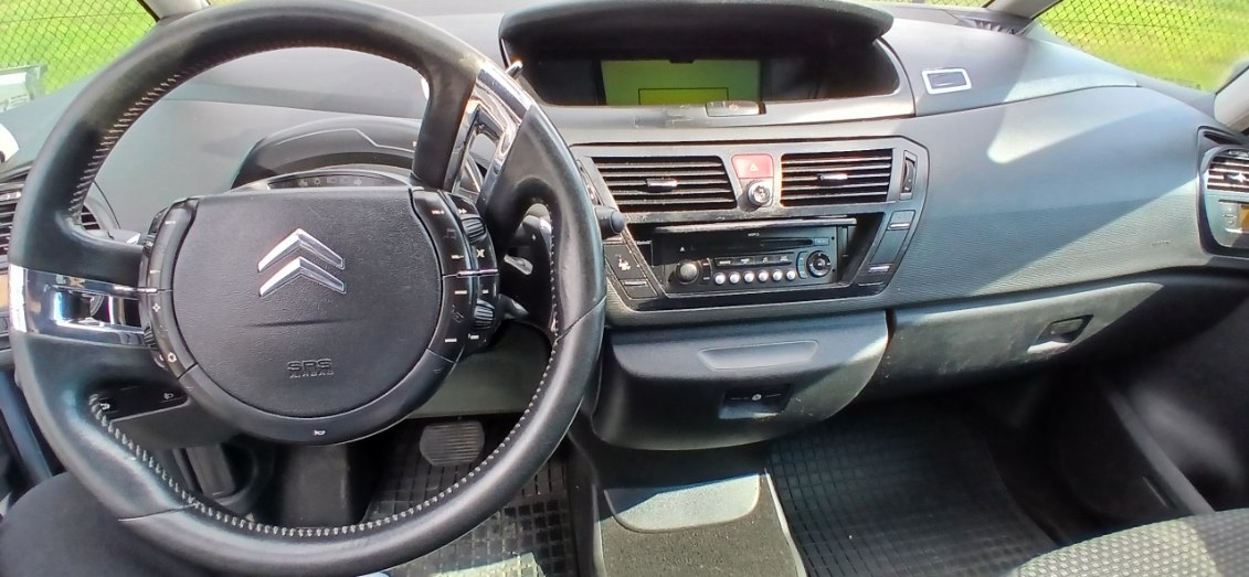 Zdjęcie przedstawia deskę rozdzielczą samochodu Citroën C4 Picasso. Kierownica z nieruchomym środkiem i centralny wyświetlacz.