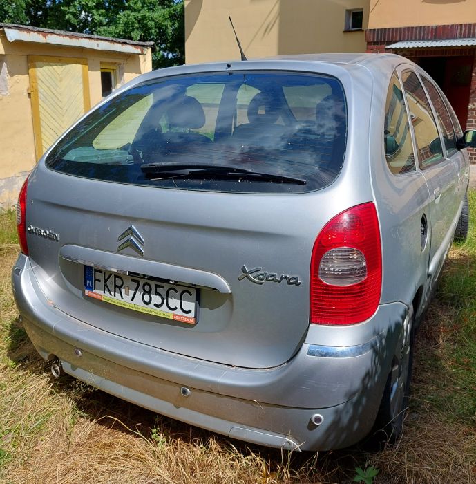 Tył i prawy bok srebrnego Citroena Xsara Picasso, widoczne otarcia zderzaka, brak klapki wlewu paliwa
