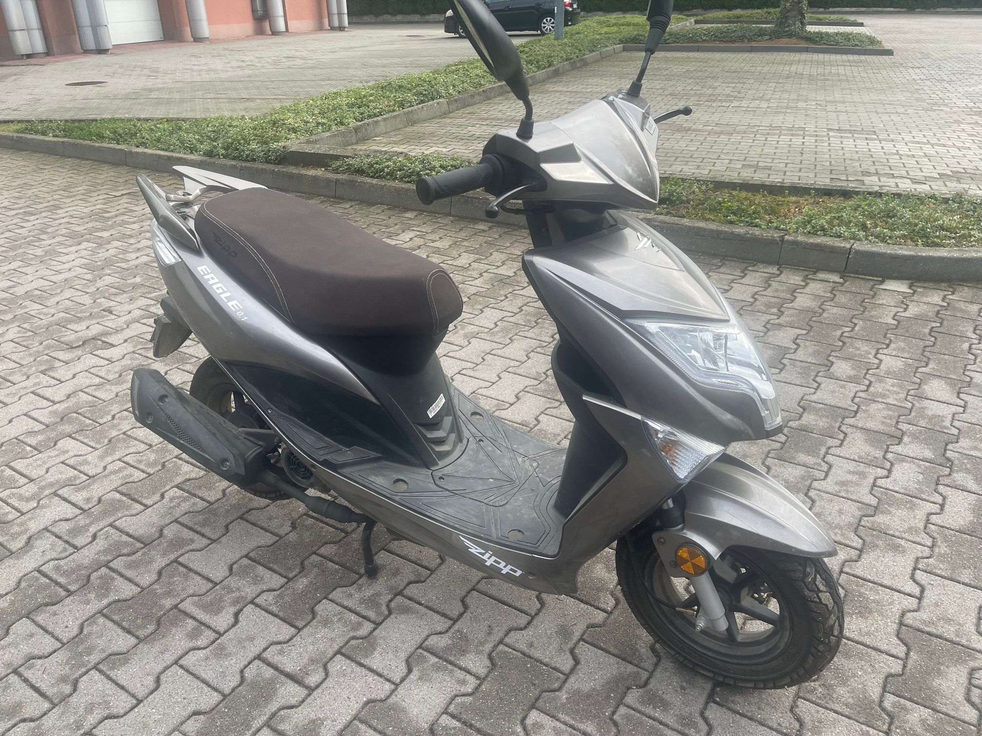 Czarno-srebrny skuter. Widoczne są przedni reflektor, dwa lusterka, kierunkowskazy, siedzenie oraz oznaczenia producenta