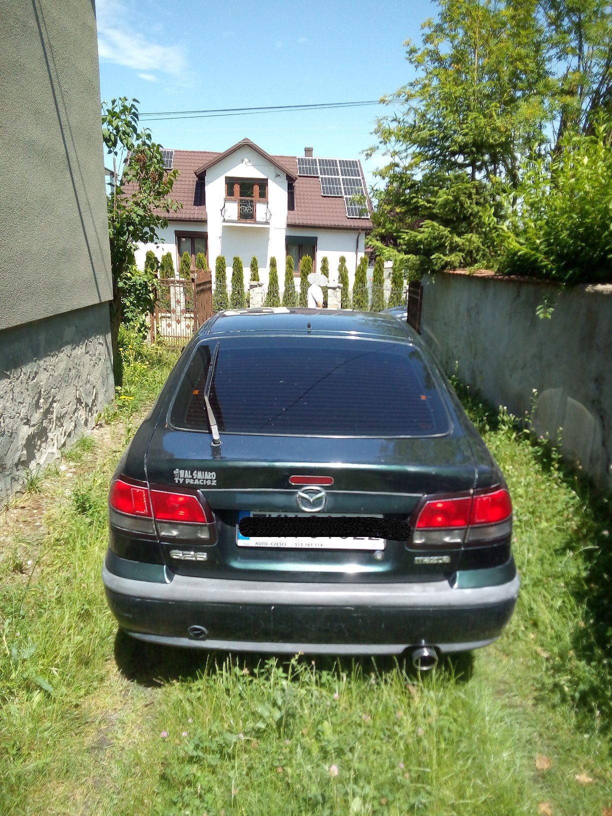 Ciemnozielony samochód osobowy marki Mazda 626 widziany od tyłu