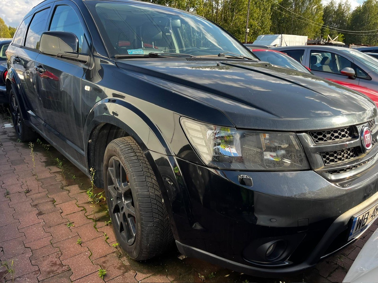 Na zdjęciu widoczny jest Fiat Freemont. Charakteryzuje się czarnym lakierem, ciemną atrapą chłodnicy oraz logo marki FIAT
