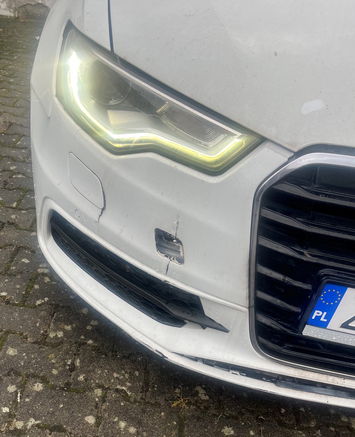 Zbliżenie przedniego zderzaka Audi A6 z uszkodzeniem mechanicznym konstrukcji tworzywa.