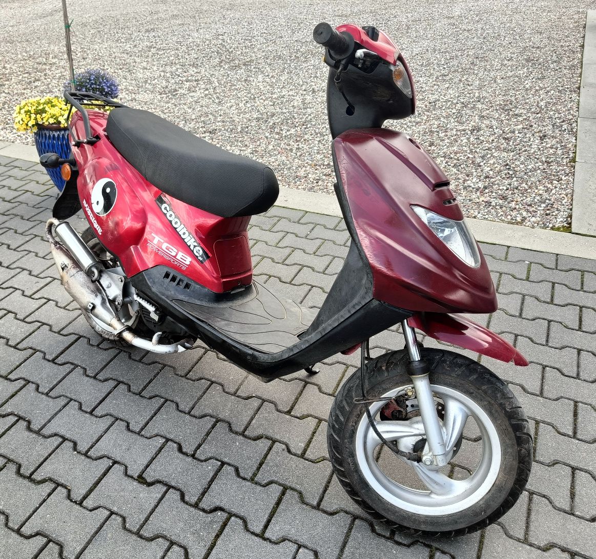 Przód oraz prawy bok motoroweru w kolorze czerwonym, widoczne zadrapania na obudowach pojazdu.