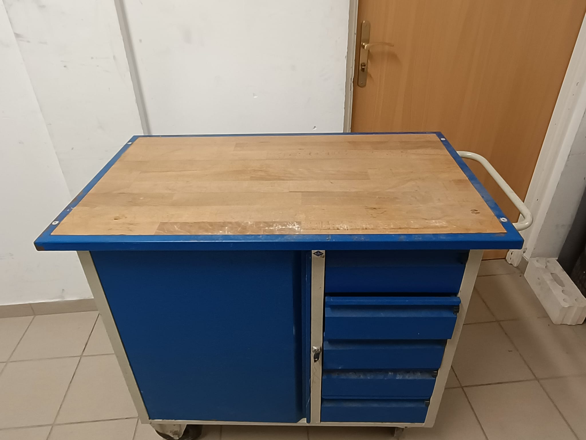 Zdjęcie przedstawia szafkę narzędziową koloru niebiesko-szarego z drewnianym blatem. Szafka używana w dobrym stanie.