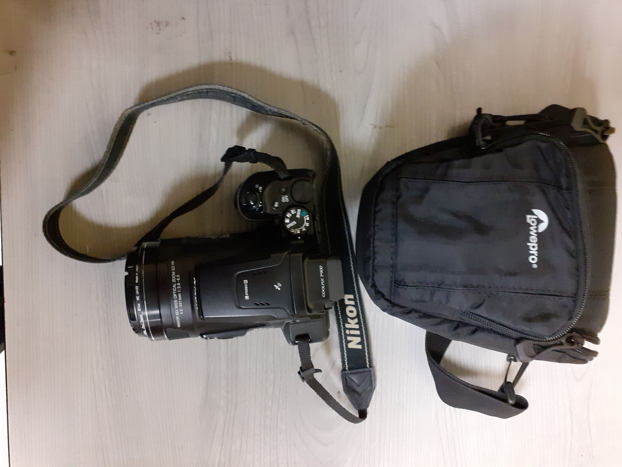 Widok z góry aparat fotograficzny w kolorze czarnym z napisem coolpix p900 wraz z futerałem w kolorze czarnym lowepro