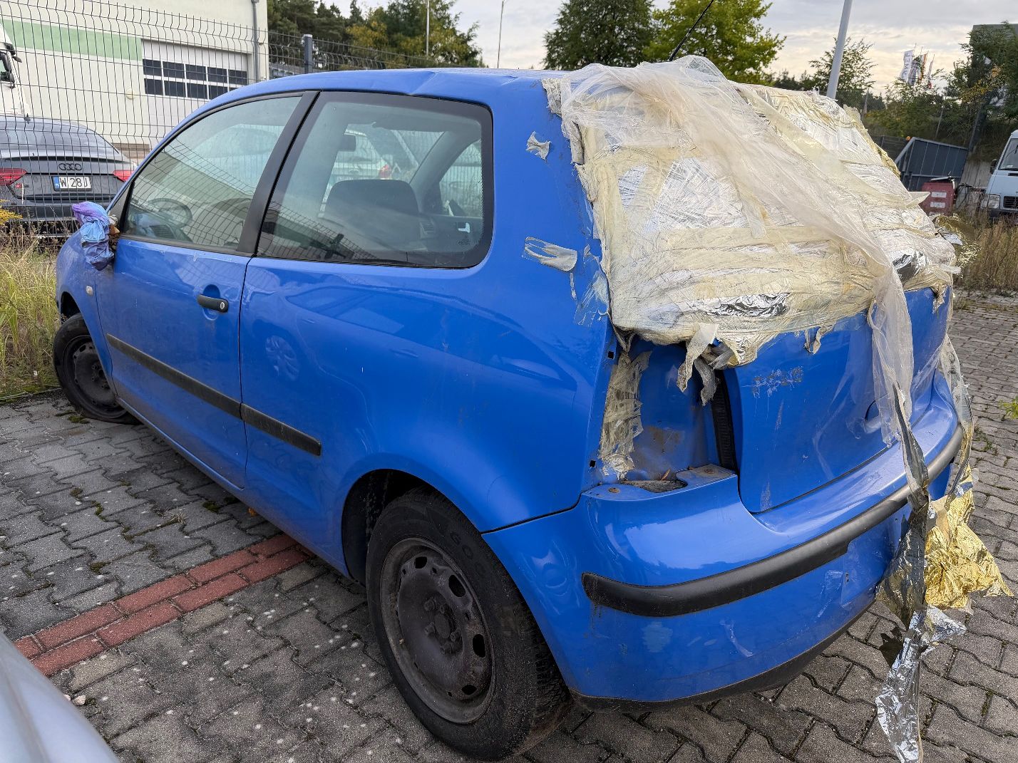 Niebieski Volkswagen Polo, widok z tyłu lewego boku, wybita tylna szyba, brak tylnej lewej lampy.