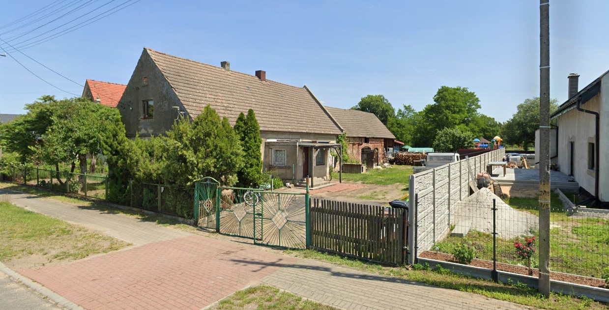 Dom z podwórkiem, zielonym płotem, otoczony drzewami i krzewami