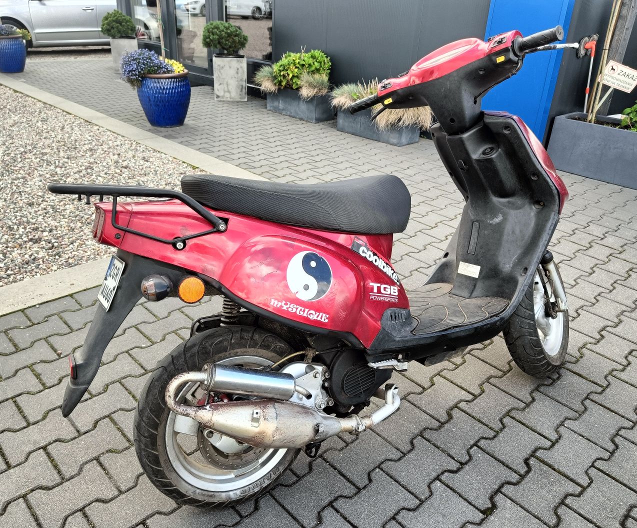 Tył oraz prawy bok motoroweru w kolorze czerwonym, widoczne zadrapania na obudowach pojazdu.