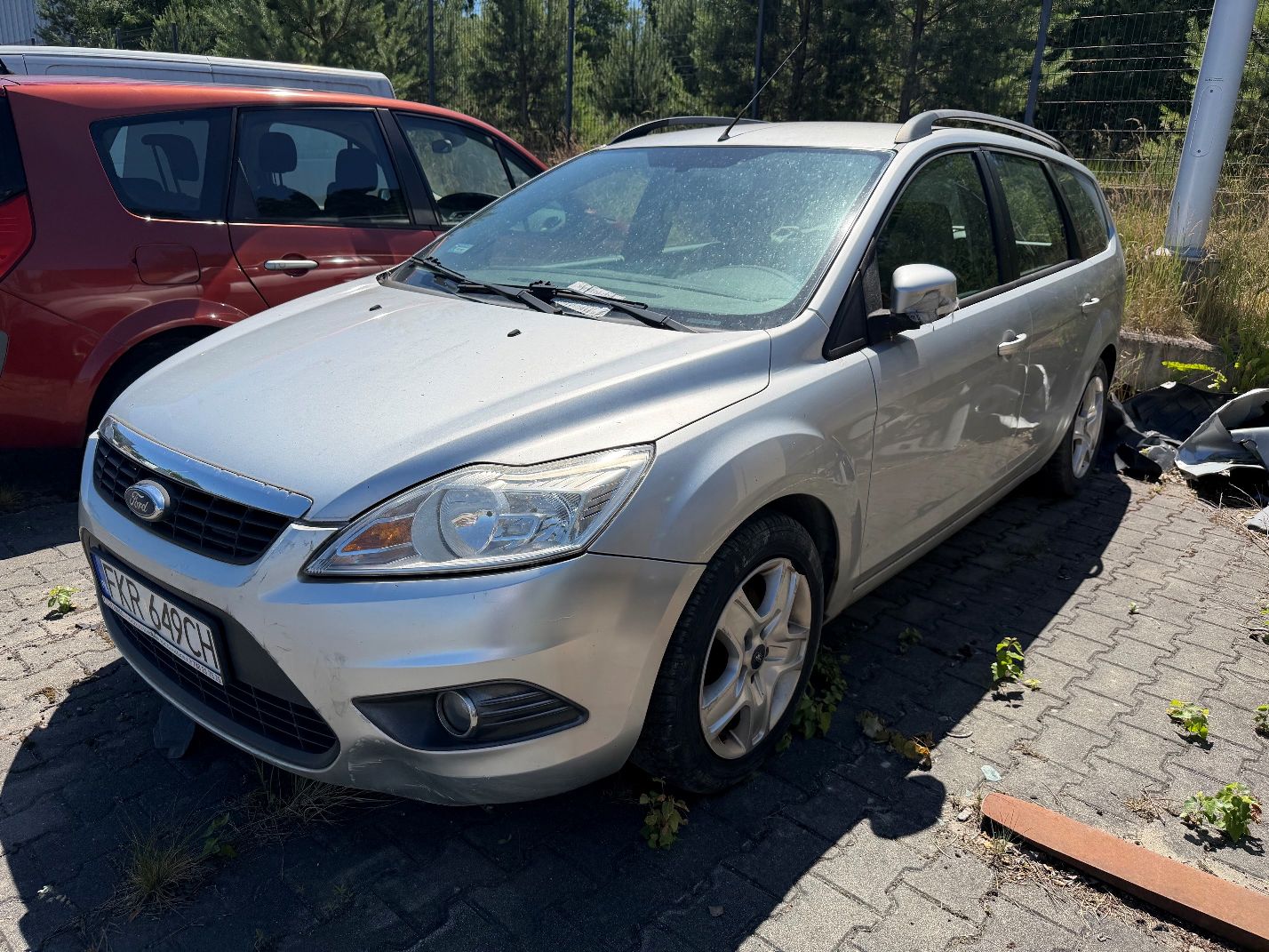 Srebrny Ford Focus, widok lewego przodu, uszkodzona lewa strona przedniego zderzaka, lusterko, lewa przednia stalowa felga