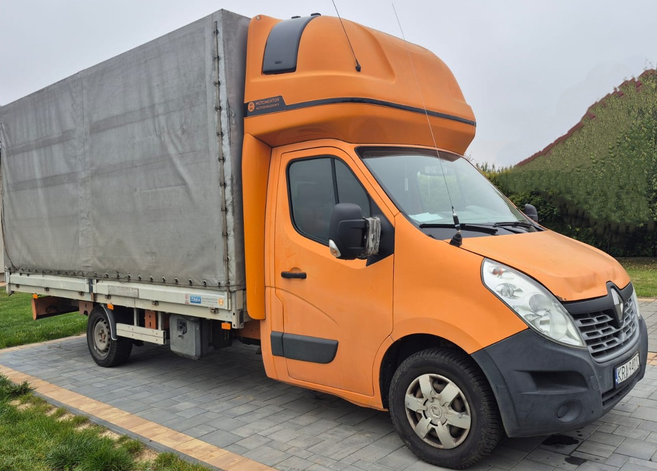 Prawa strona pojazdu Renault Master koloru pomarańczowego z szarą plandeką. Uszkodzone lusterko boczne.
