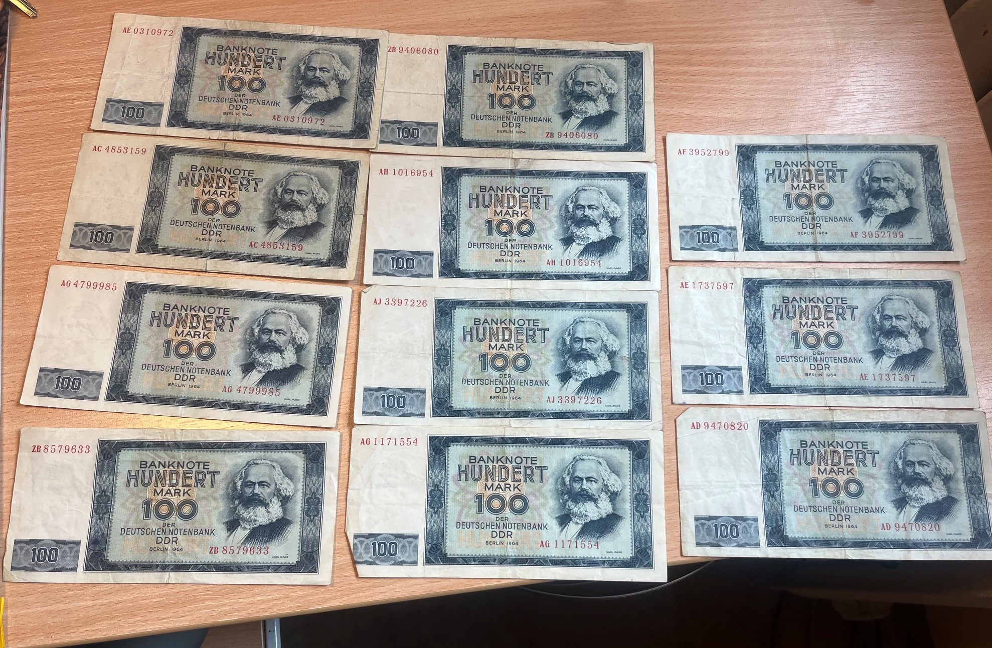 Kolekcja jedenastu banknotów o nominale 100 marek NRD z 1964 roku ułożonych w rzędach.