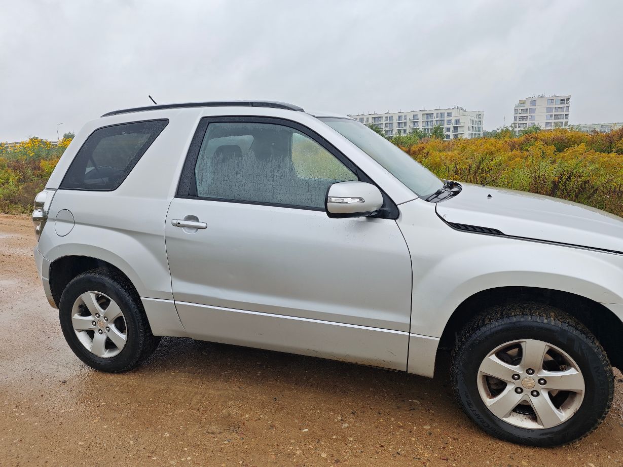 Srebrny samochód marki Suzuki Grand Vitara II w wersji trzydrzwiowej, prawy bok