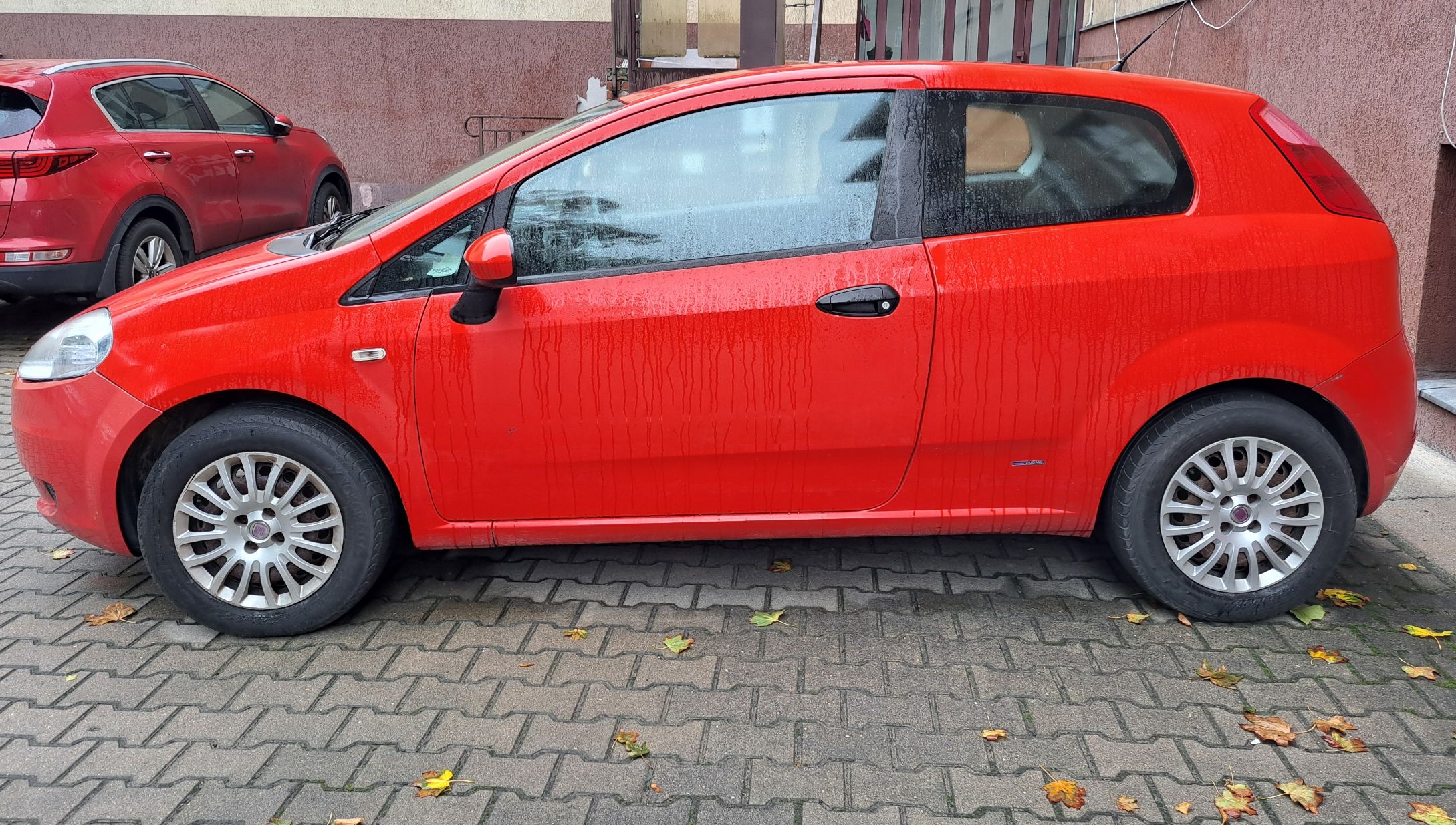 lewa strona czerwonego samochodu osobowego Fiata Punto przebarwienia lakieru lekkie zadrapania na drzwiach
