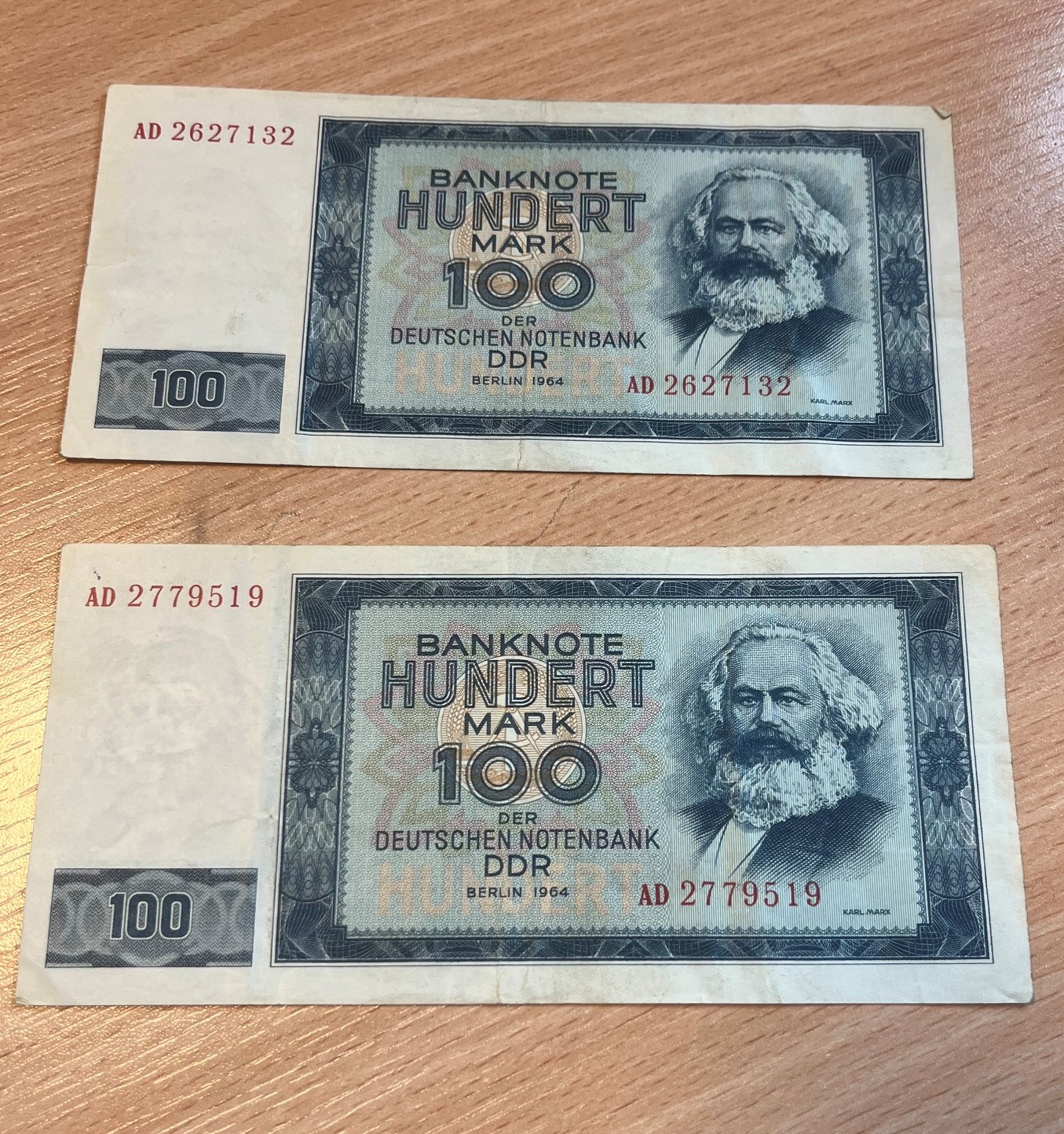 Dwa banknoty o nominale 100 marek NRD z emisji z 1964 roku ułożone pionowo jeden pod drugim.