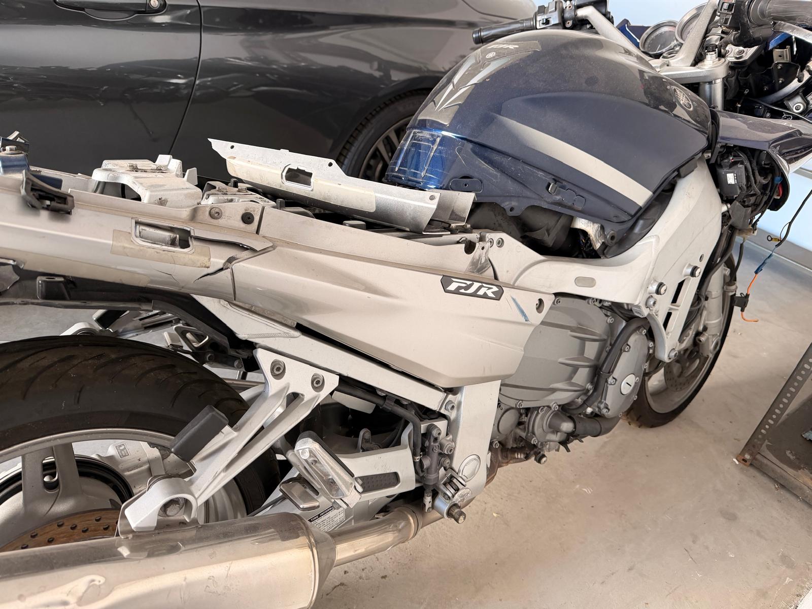 Bok granatowego motocykla Yamaha FJR z widocznymi uszkodzeniami. Pojazd zaparkowany w garażu.
