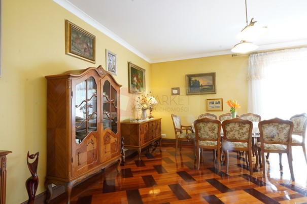 przestronny salon, z dużym stołem i krzesłami, stylowa komoda w kolorze brązowym, parkiet mahoniowy na wysoki połysk