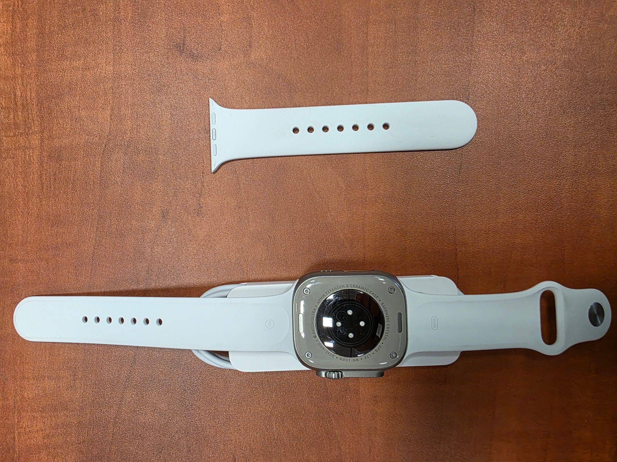 Apple Watch Ultra seria 1 koloru białego z częścią opaski koloru białego i kablem zasilającym koloru białego - strona tylna