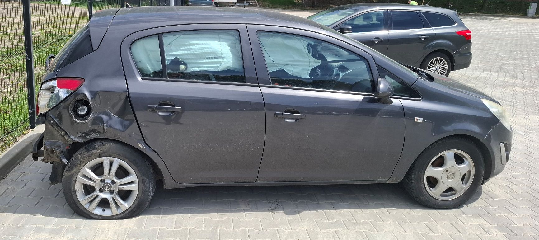 Grafitowy Opel Corsa, widok z prawego boku, widoczne uszkodzenia tylnego lewego narożnika nadwozia.