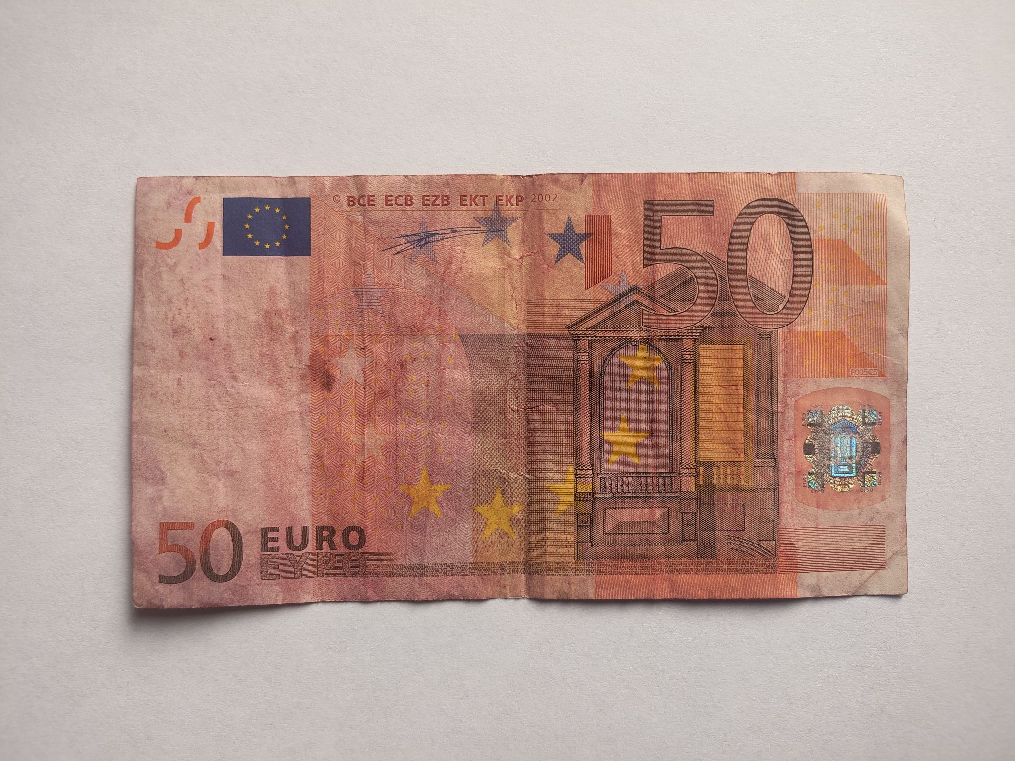 Zużyty i odbarwiony rewers tego samego banknotu, przedstawiający architekturę w stylu renesansowym.
