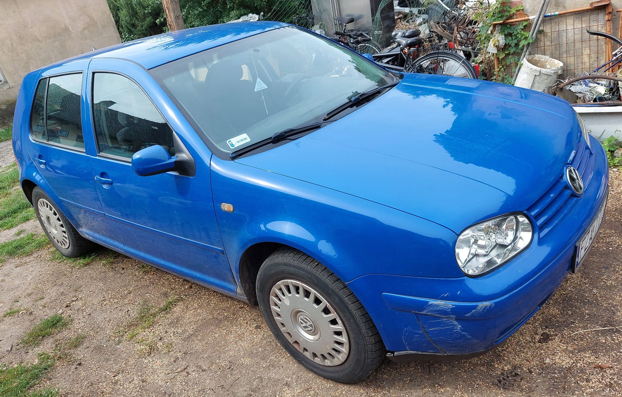 Przód i lewy bok niebieskiego Volkswagena Golfa, widoczne otarcia na zderzaki.