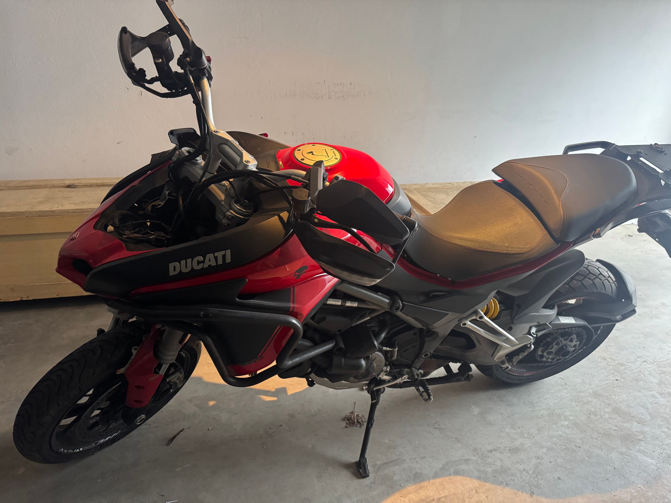 Przód czerwonego Ducati Multistrada. Motocykl stojący na bocznej stopce w garażu.