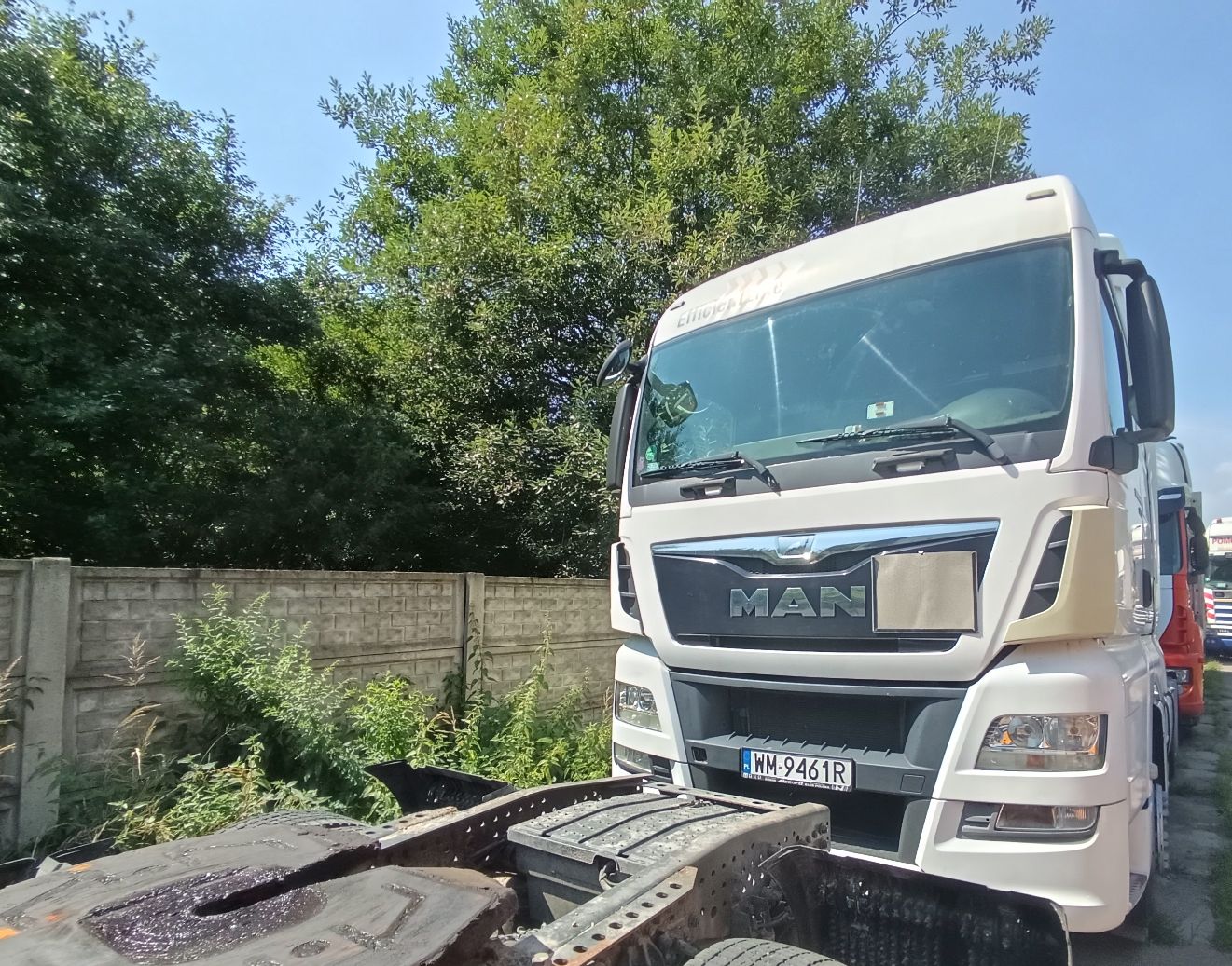 Biały ciągnik siodłowy ciężarowy widziany z przodu. Charakterystyczny grill z dużym logo marki MAN.