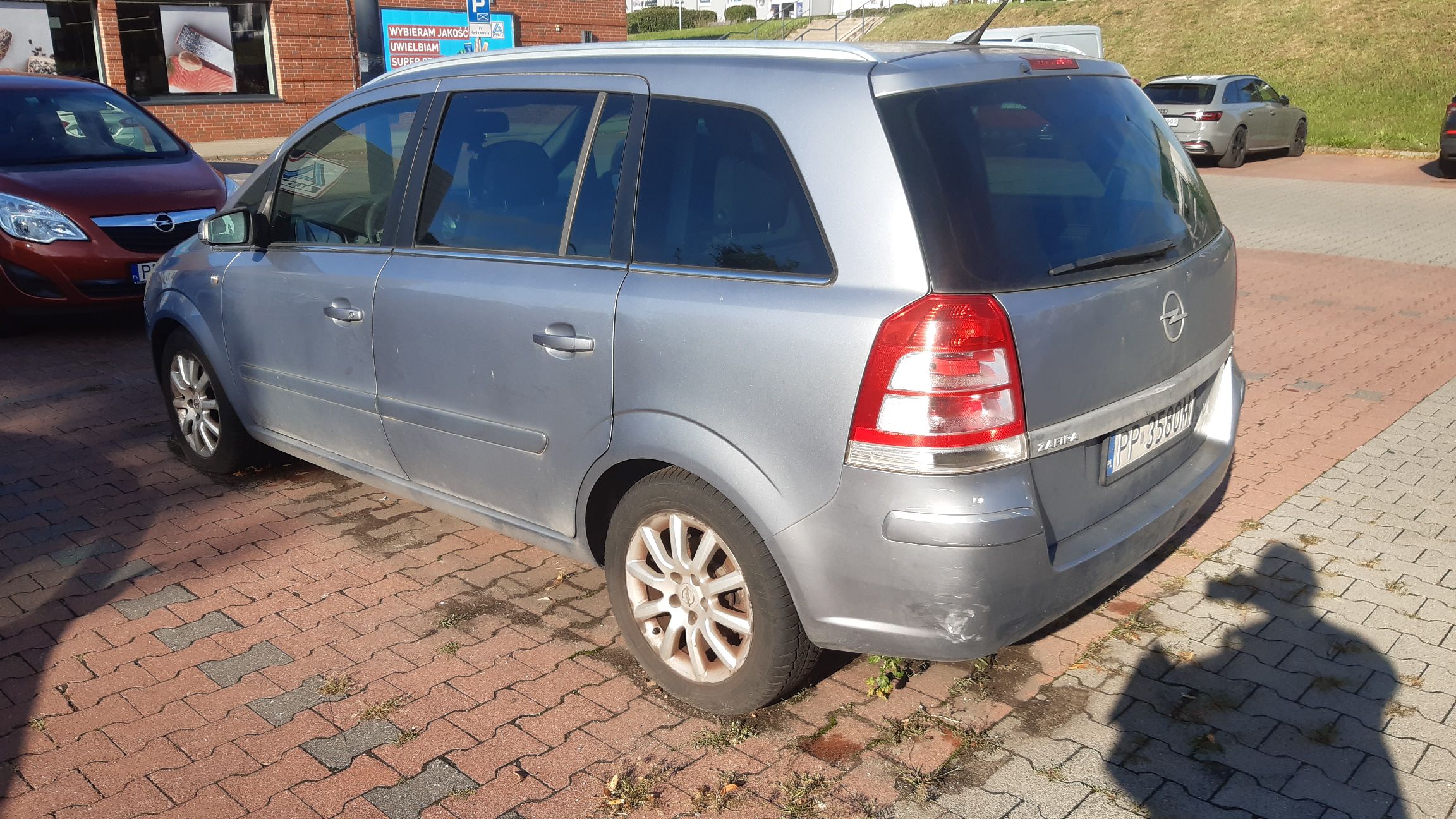Srebrny samochód osobowy Opel Zafira, sfotografowany z tytułu i z prawej strony