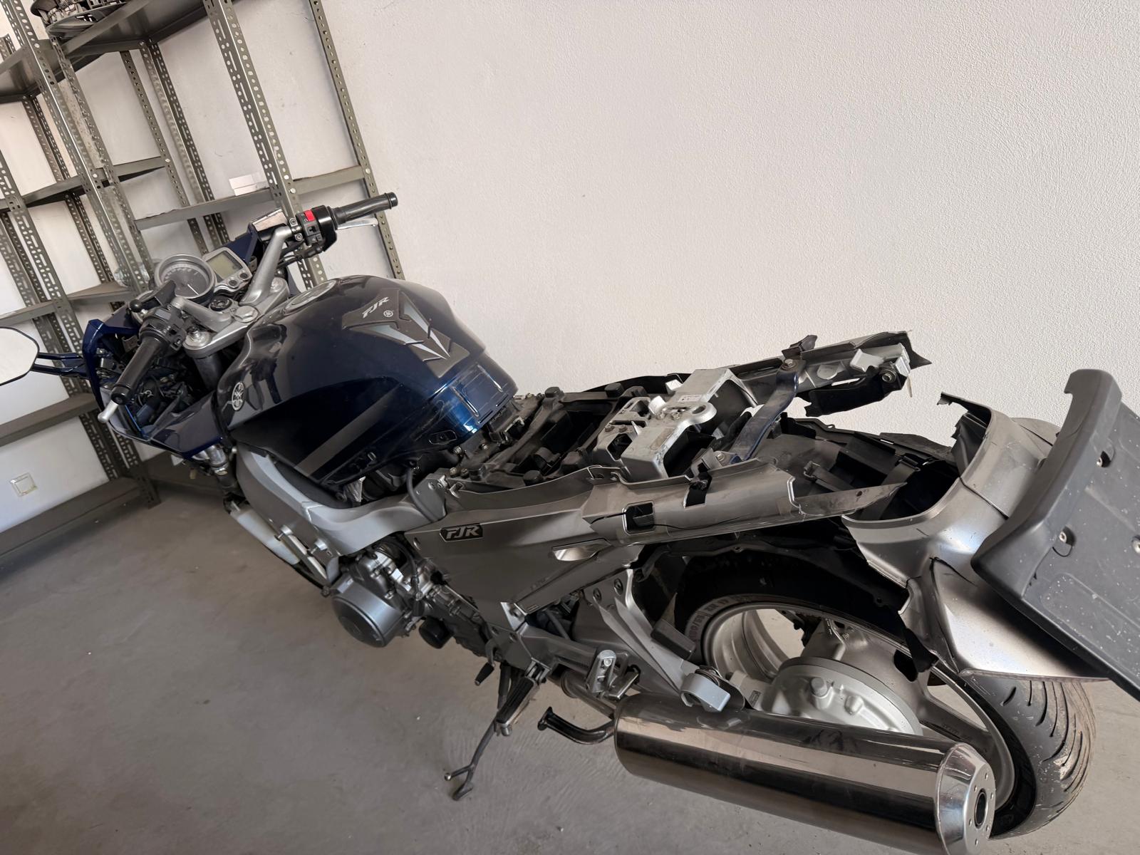 Bok granatowego motocykla Yamaha FJR z widocznymi uszkodzeniami. Pojazd zaparkowany w garażu.