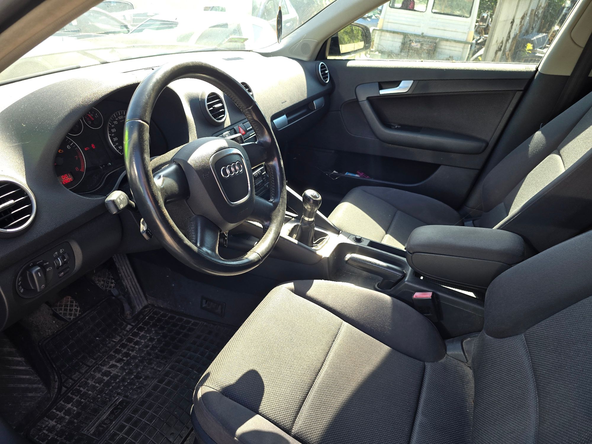 Wnętrze granatowego samochodu Audi A3. Widoczna kierownica z logo marki, deska rozdzielcza, fotele oraz przednia i boczna szyba.