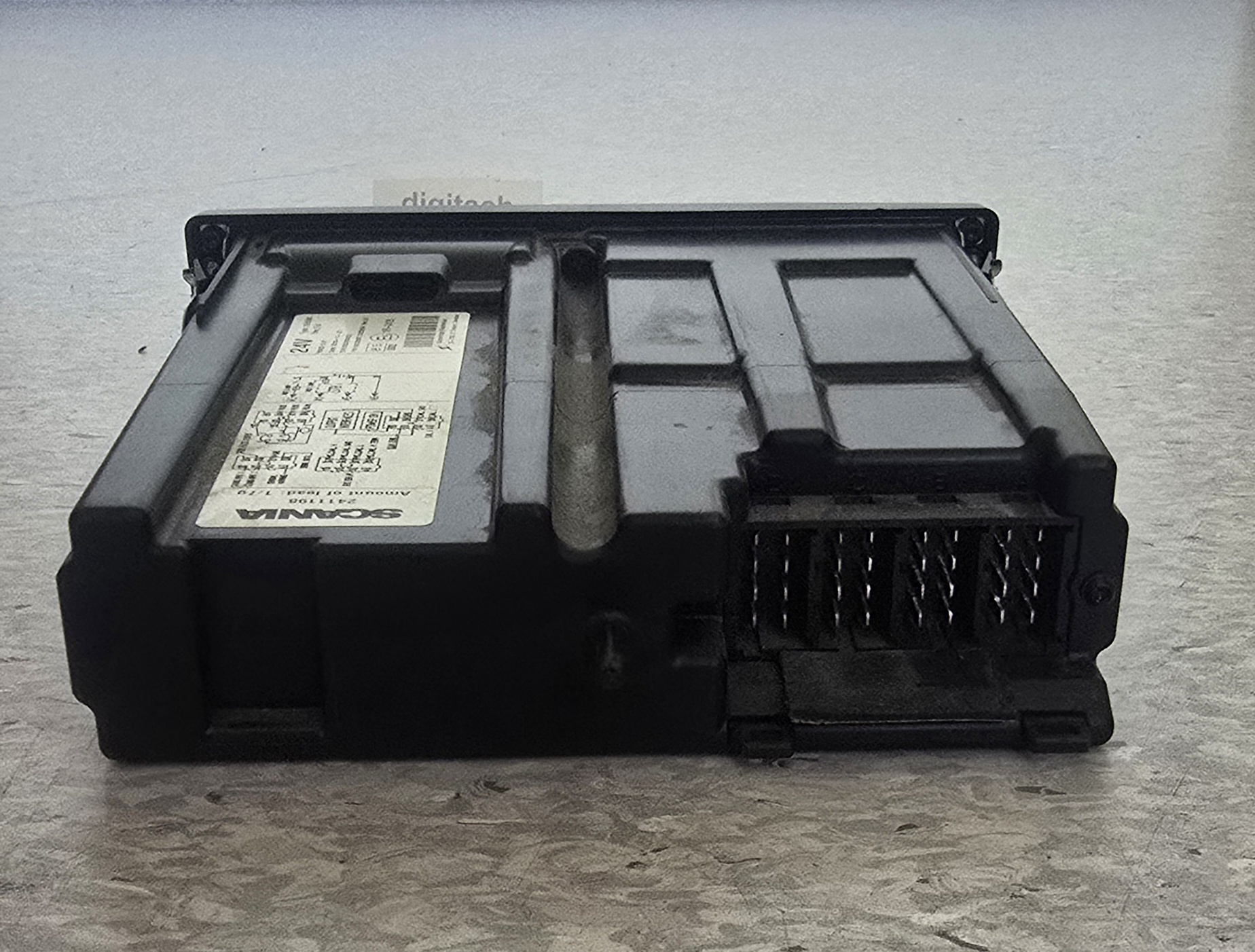 Czarny moduł elektroniczny, sterownik pojazdu, z widocznym złączem pinowym i naklejką z danymi technicznymi.