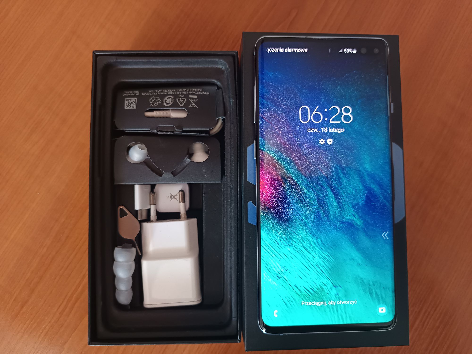 Smartfon z akcesoriami: ładowarką, przewodem USB, słuchawkami i narzędziem do wyjmowania karty SIM.
